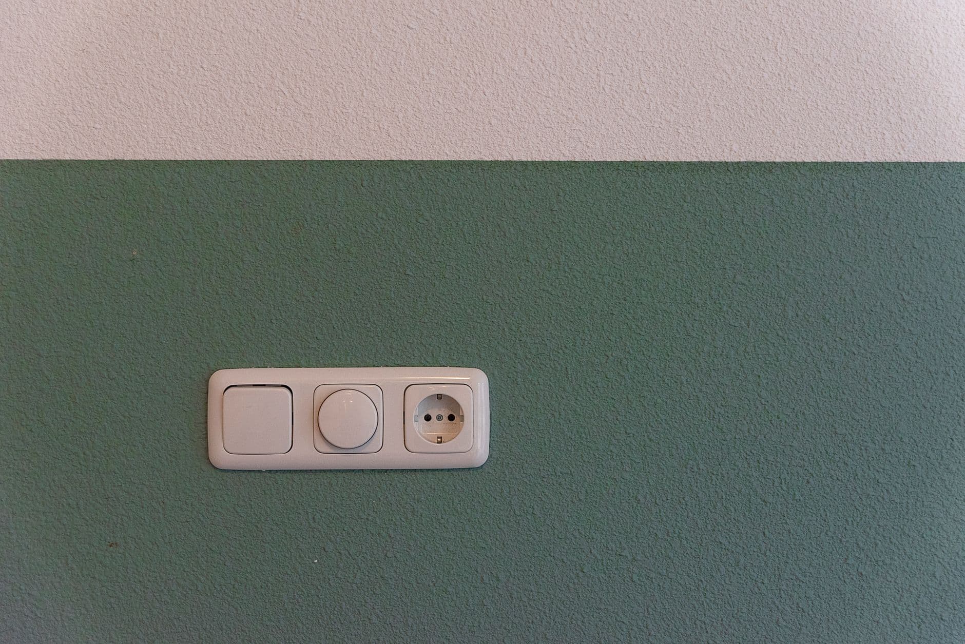A switch, a dimmer and a socket on one plate on a green wall.