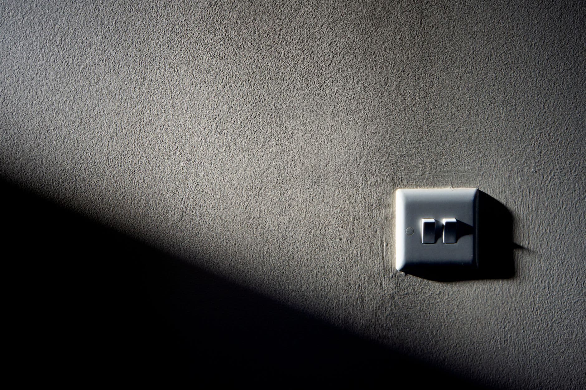 A wall light switch half in shadow on a textured wall.
